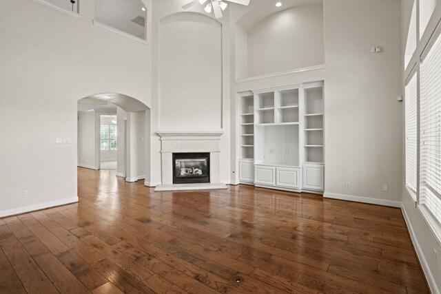 unfurnished living room featuring a high ceiling, dark hardwood / wood-style floors, ceiling fan, and plenty of natural light