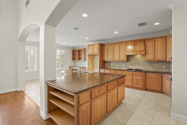 kitchen with an island with sink, gas stovetop, crown molding, light hardwood / wood-style flooring, and sink