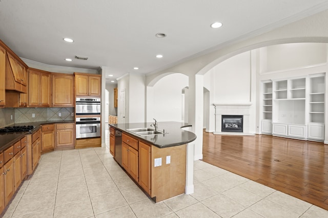 kitchen with sink, a center island with sink, a tiled fireplace, stainless steel appliances, and light hardwood / wood-style floors