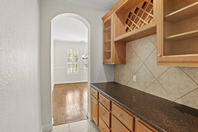 kitchen with light hardwood / wood-style floors, ornamental molding, dark stone countertops, and tasteful backsplash