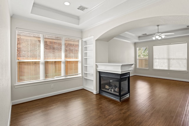 unfurnished living room with a tray ceiling, a multi sided fireplace, dark hardwood / wood-style flooring, ornamental molding, and ceiling fan