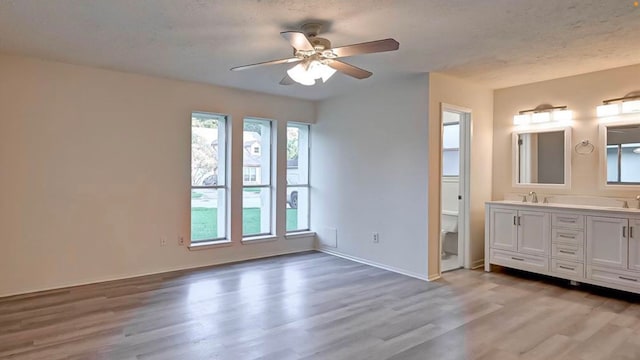 unfurnished bedroom featuring ceiling fan, sink, a textured ceiling, light hardwood / wood-style flooring, and ensuite bathroom