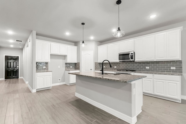 kitchen with white cabinets, a center island with sink, stone counters, stainless steel appliances, and light hardwood / wood-style floors