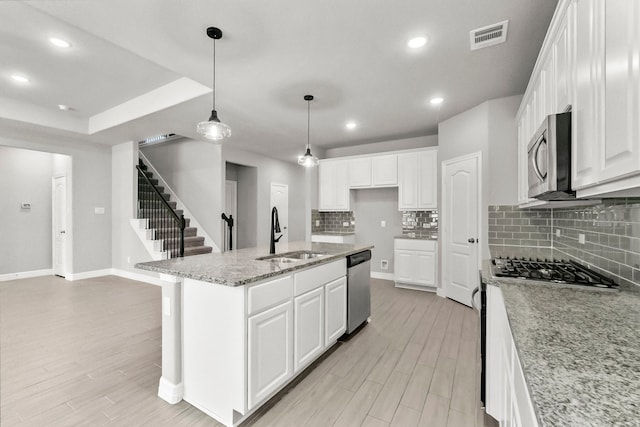 kitchen featuring an island with sink, white cabinets, light stone countertops, stainless steel appliances, and sink