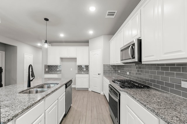 kitchen with white cabinets, stainless steel appliances, sink, and light stone countertops