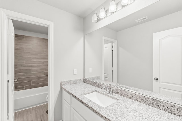 full bathroom featuring hardwood / wood-style floors, tiled shower / bath, vanity, and toilet