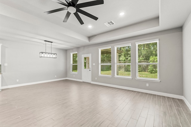 empty room with light hardwood / wood-style flooring, a tray ceiling, and ceiling fan