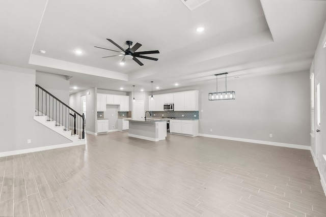 unfurnished living room featuring light hardwood / wood-style flooring, ceiling fan, a raised ceiling, and sink