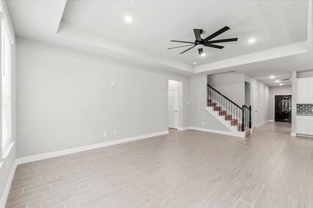 empty room with a tray ceiling, ceiling fan, and light hardwood / wood-style flooring