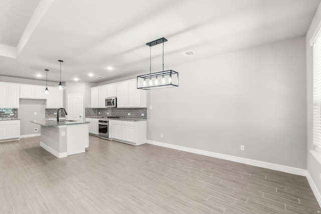 kitchen with an island with sink, white cabinetry, hanging light fixtures, and sink