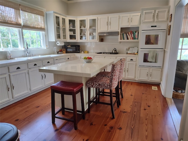 kitchen with white double oven, sink, dark wood-type flooring, and white cabinets