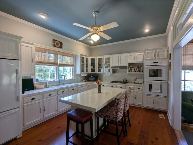 kitchen with a kitchen breakfast bar, white cabinetry, white appliances, ceiling fan, and sink