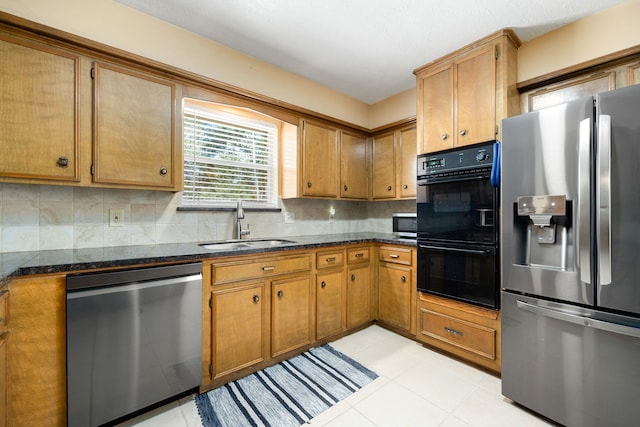 kitchen with appliances with stainless steel finishes, dark stone countertops, backsplash, light tile patterned floors, and sink