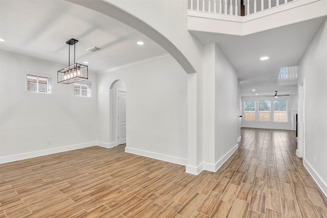 interior space featuring a high ceiling, ceiling fan with notable chandelier, light hardwood / wood-style flooring, and ornamental molding