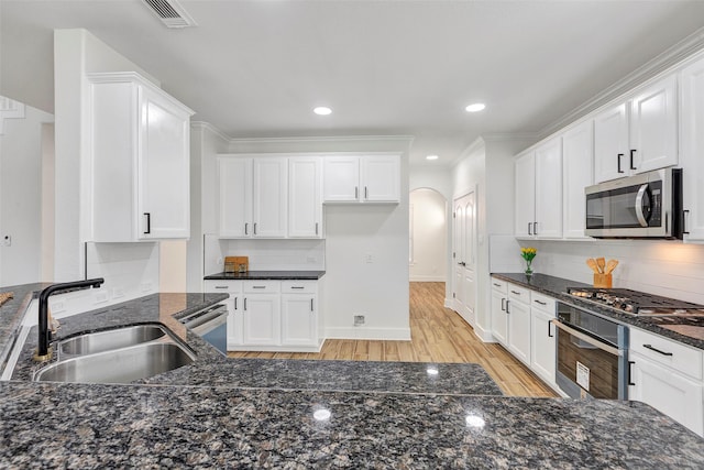 kitchen with sink, dark stone countertops, light wood-type flooring, white cabinetry, and stainless steel appliances