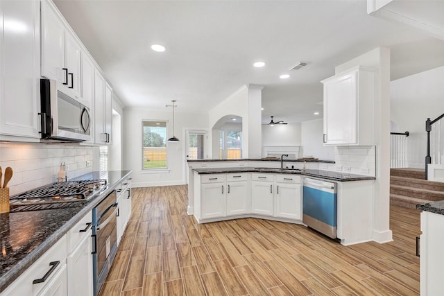 kitchen featuring white cabinets, stainless steel appliances, hanging light fixtures, and light hardwood / wood-style flooring