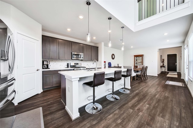 kitchen featuring a center island with sink, sink, appliances with stainless steel finishes, decorative light fixtures, and dark brown cabinets