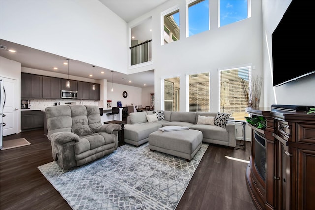 living room featuring a towering ceiling, a healthy amount of sunlight, and dark hardwood / wood-style floors