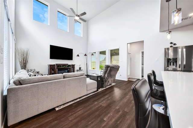 living room featuring a fireplace, a high ceiling, dark hardwood / wood-style flooring, and ceiling fan