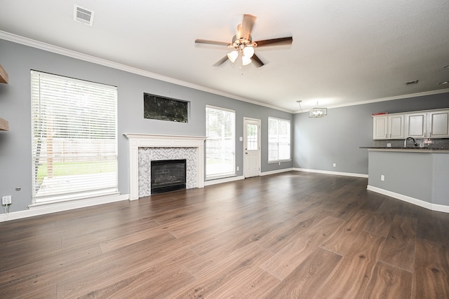 unfurnished living room with ceiling fan with notable chandelier, wood-type flooring, a tiled fireplace, and crown molding