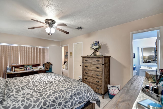 bedroom featuring ceiling fan, light colored carpet, a textured ceiling, and connected bathroom