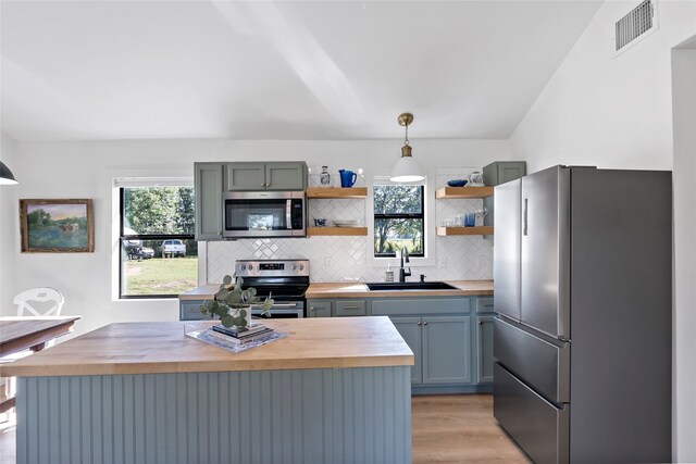 kitchen with sink, butcher block counters, hanging light fixtures, light hardwood / wood-style flooring, and appliances with stainless steel finishes