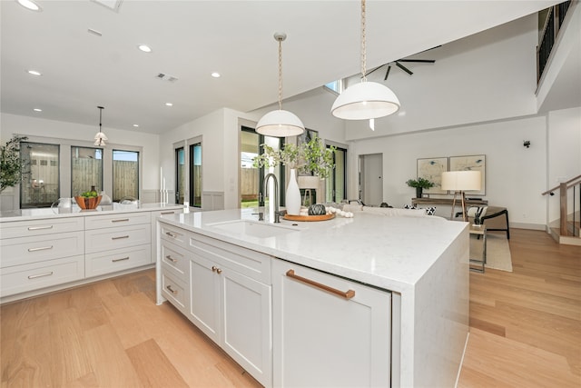 kitchen with hanging light fixtures, a kitchen island with sink, sink, and light hardwood / wood-style flooring