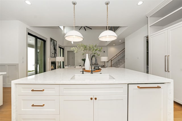 kitchen with light hardwood / wood-style floors, sink, white cabinets, decorative light fixtures, and light stone countertops