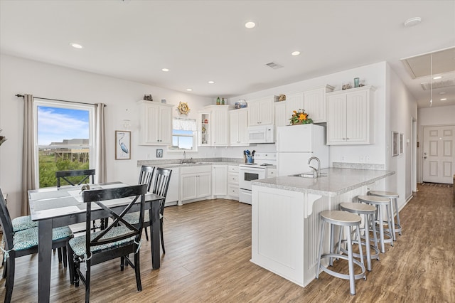 kitchen with white cabinetry, a kitchen bar, a kitchen island, light hardwood / wood-style flooring, and white appliances