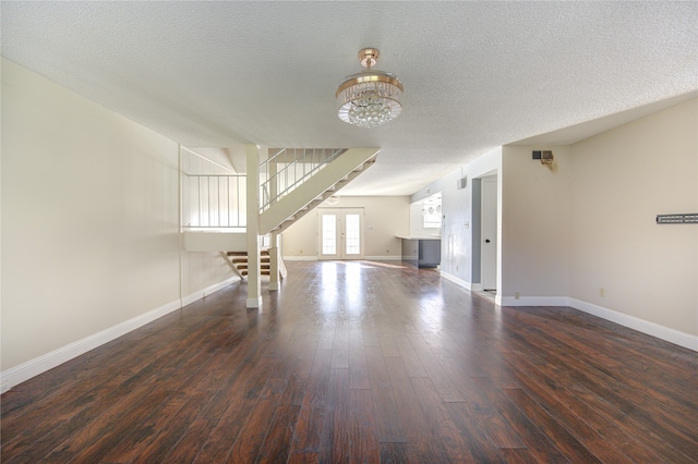 unfurnished living room with a textured ceiling, dark hardwood / wood-style flooring, french doors, and a notable chandelier