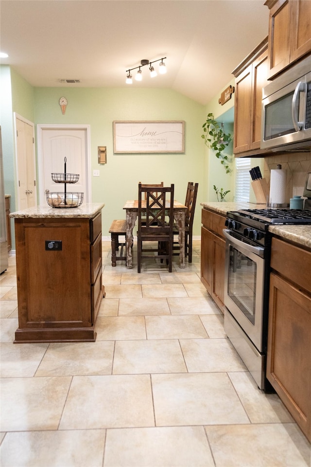 kitchen with light tile patterned floors, tasteful backsplash, a kitchen island, stainless steel appliances, and vaulted ceiling