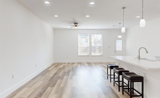 kitchen featuring sink, light hardwood / wood-style floors, a center island with sink, decorative light fixtures, and a kitchen breakfast bar