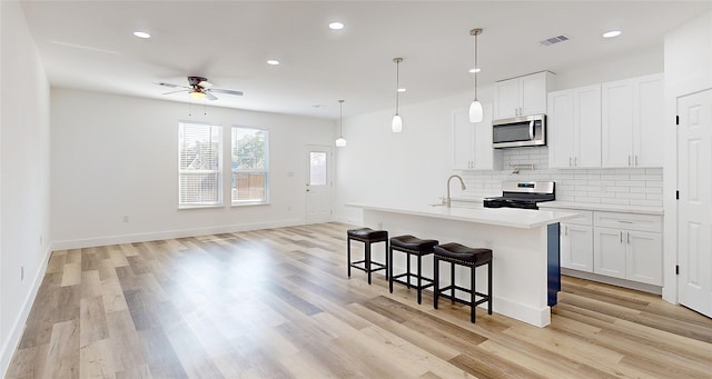 kitchen featuring an island with sink, light hardwood / wood-style flooring, decorative light fixtures, white cabinetry, and stainless steel appliances