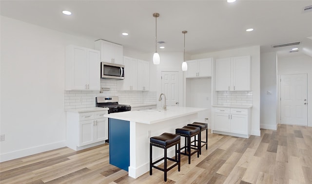 kitchen with light wood-type flooring, sink, stainless steel appliances, an island with sink, and white cabinetry