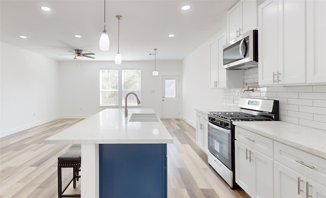 kitchen featuring pendant lighting, light hardwood / wood-style flooring, sink, stainless steel appliances, and white cabinetry