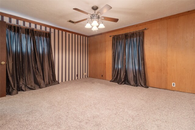 carpeted empty room featuring ceiling fan, a textured ceiling, and wooden walls