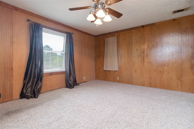 carpeted empty room featuring ceiling fan and wood walls