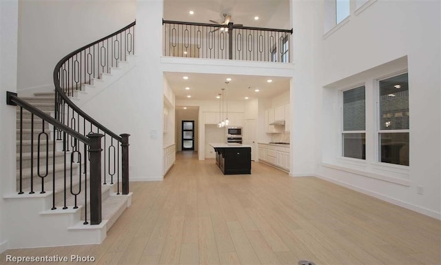 interior space featuring a notable chandelier, light wood-type flooring, and a towering ceiling