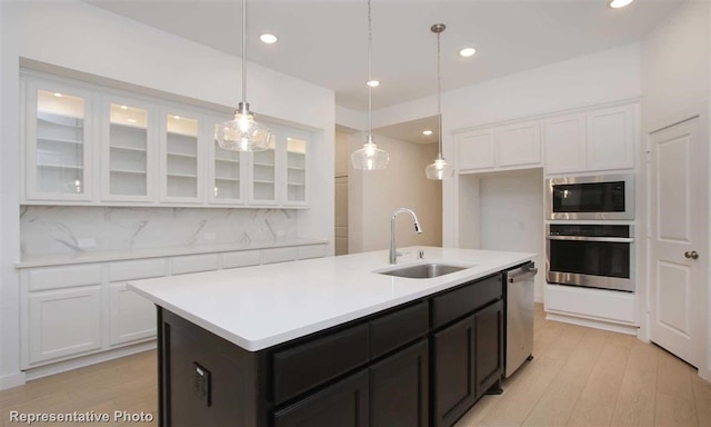 kitchen featuring sink, backsplash, stainless steel appliances, light hardwood / wood-style flooring, and a kitchen island with sink