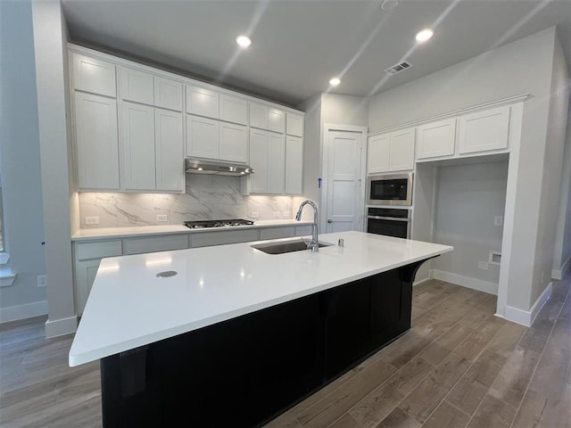 kitchen with stainless steel appliances, tasteful backsplash, white cabinets, a sink, and under cabinet range hood