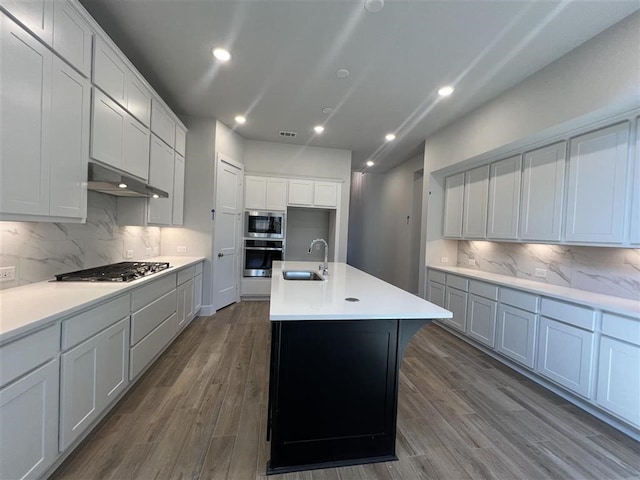 kitchen with stainless steel appliances, a sink, under cabinet range hood, and dark wood-style floors