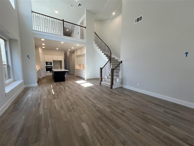 unfurnished living room with visible vents, dark wood-type flooring, a sink, baseboards, and stairs