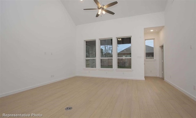 spare room with high vaulted ceiling, light wood-style floors, baseboards, and a ceiling fan