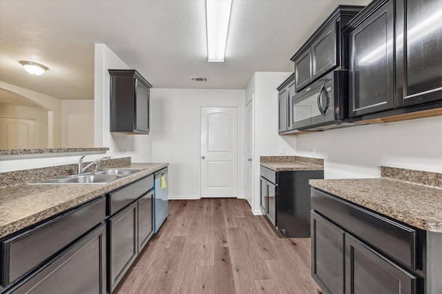 kitchen featuring a textured ceiling, stainless steel dishwasher, sink, and light hardwood / wood-style flooring