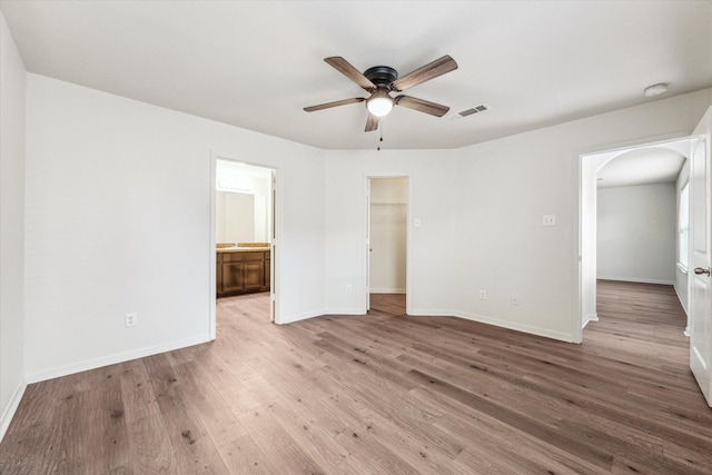 unfurnished bedroom featuring a closet, light hardwood / wood-style flooring, ensuite bath, a spacious closet, and ceiling fan