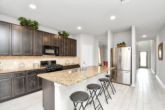 kitchen featuring a breakfast bar, a kitchen island with sink, sink, black appliances, and light stone countertops