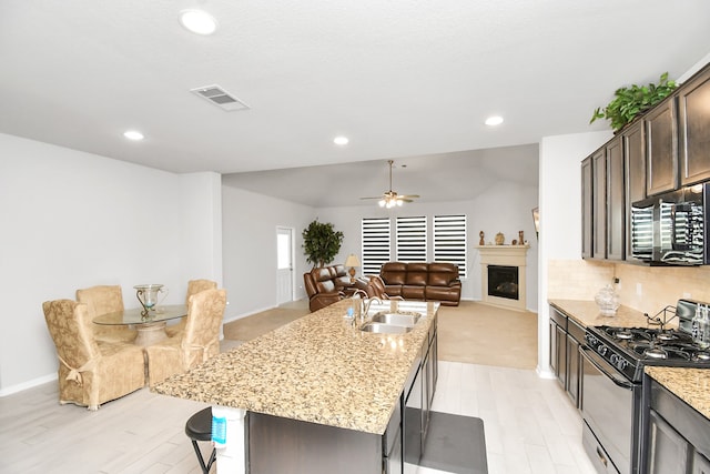 kitchen featuring dark brown cabinets, sink, an island with sink, black appliances, and ceiling fan