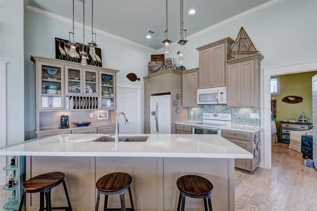 kitchen with pendant lighting, a breakfast bar, white appliances, a kitchen island with sink, and sink