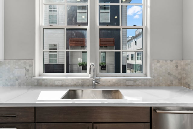 kitchen with dark brown cabinets, stainless steel dishwasher, sink, and light stone counters