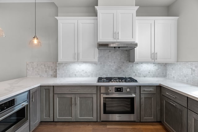 kitchen featuring pendant lighting, white cabinetry, stainless steel appliances, dark hardwood / wood-style floors, and light stone countertops